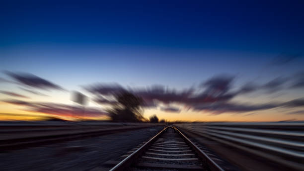istock Railway station with motion blur effect. Blurred railroad. Industrial conceptual landscape with blurred railway station, buildings, blue sky with colorful clouds and sun. Railway track 1124396101