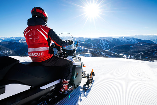 First responder enjoying a beautiful snow-caped mountain ridge while sitting on his two seater snowmobile.\n\nNOTE TO INSPECTION: problem content removed, please revise.