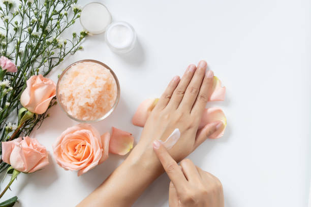 natürliche hautpflege-konzept. frau weiß creme auf ihre hände auf weißem hintergrund mit glas kosmetische creme, salz spa peeling, rosa und weißen blüten mit textfreiraum - jar human hand moisturizer packaging stock-fotos und bilder