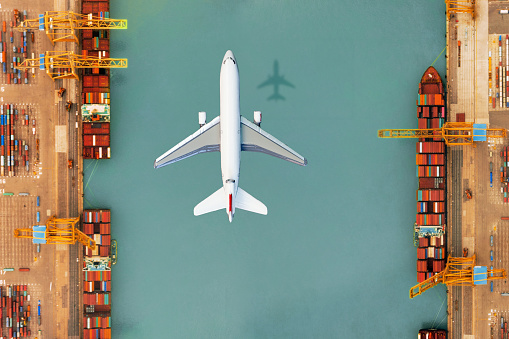 Airplane flying over container port.