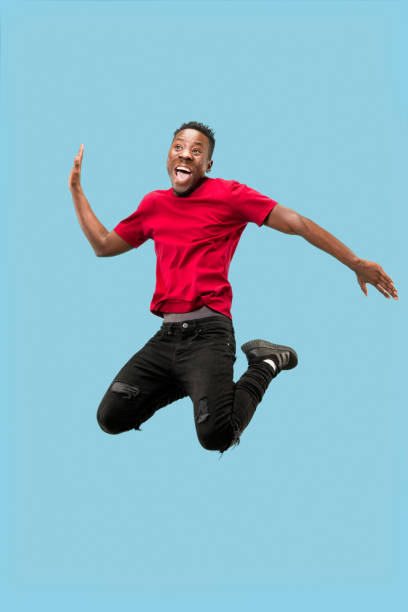 libertad en el movimiento de avance y movimiento. el hombre afro joven sorprendido feliz saltando - hip expressing positivity full blue fotografías e imágenes de stock