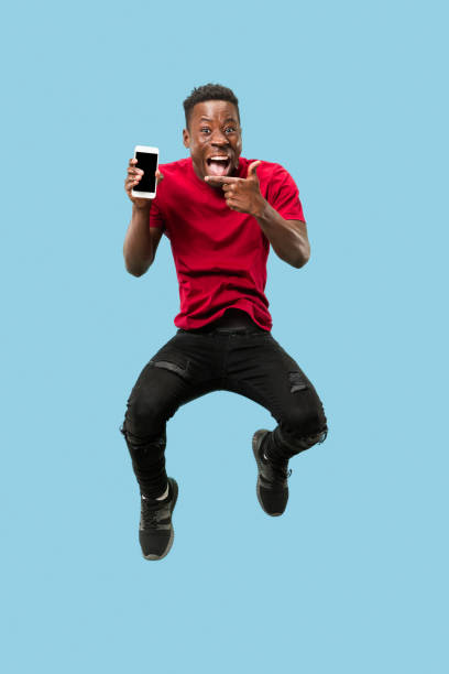 istock always on mobile. Full length of handsome young man taking phone while jumping 1124411592