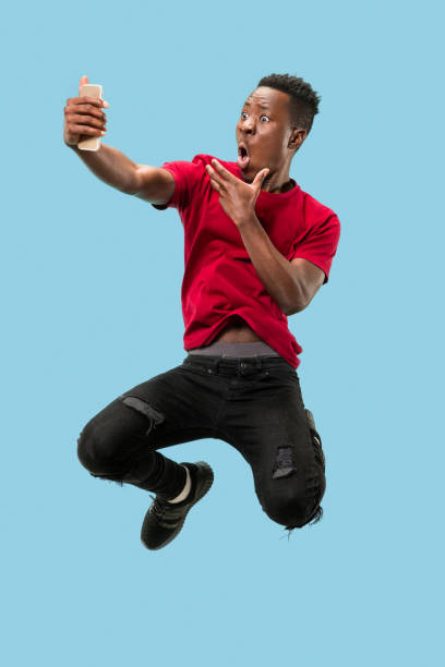 istock always on mobile. Full length of handsome young man taking phone while jumping 1124411613