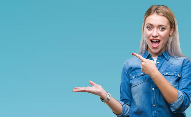 istock Young blonde woman over isolated background amazed and smiling to the camera while presenting with hand and pointing with finger. 1124412980