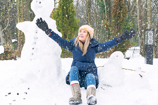Woman enjoying with snow, making snowman in woods