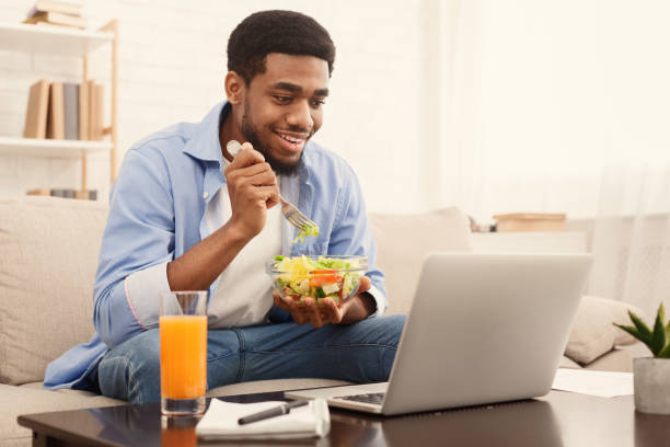 Black man eating vegetable salad at laptop