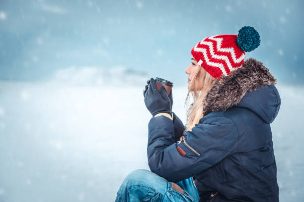 nettes mädchen draußen sitzen auf einem verschneiten wintertag - tea island stock-fotos und bilder