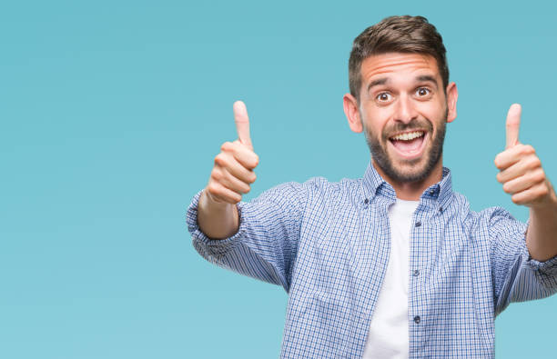 istock Young handsome man wearing white t-shirt over isolated background approving doing positive gesture with hand, thumbs up smiling and happy for success. Looking at the camera, winner gesture. 1124427477