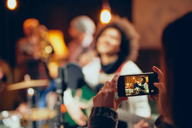 Photo of Woman taking photo of the band on rehearsal with smart phone.