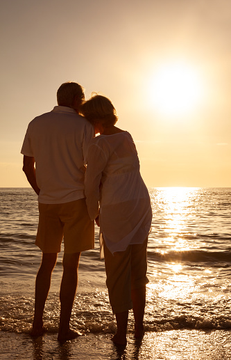 Romantic senior man and woman couple holding hands embracing at sunset or sunrise on a deserted tropical beach