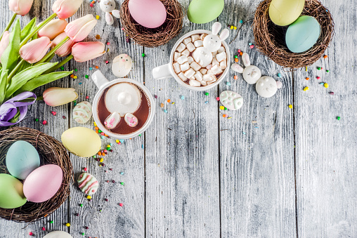 Easter funny kids food and drink concept, sweet hot chocolate with marshmallow bunny rabbits and easter eggs, wooden background copy space top view