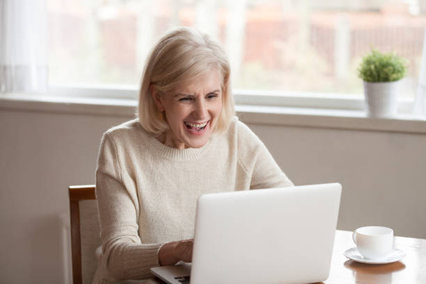 istock Cheerful senior female sitting at table watching video on pc 1124436501