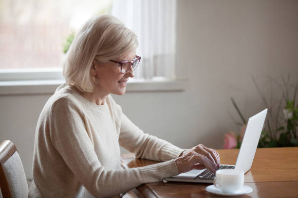 istock Satisfied mature woman typing message using notebook sitting at table 1124436538