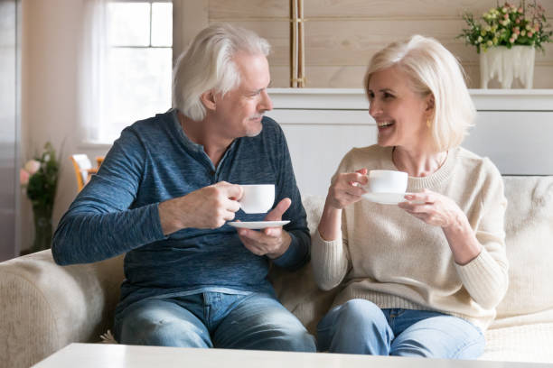 istock Smiling couple middle aged people sitting on couch drinking tea 1124436621