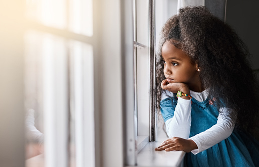 Shot of an adorable little girl looking out the window at home