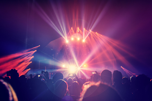 Large group of a happy young people enjoying concert, having fun spending time in a night club, dancing in bright laser beams, men partying, celebrating holidays