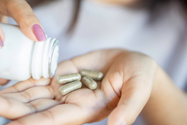 mão de mulher tomando comprimidos de medicamento de erva - capsule vitamin pill pill nutritional supplement - fotografias e filmes do acervo