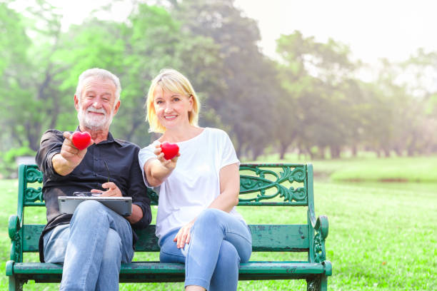 Happy senior couple in park holding heart in love valentine day concept stock photo