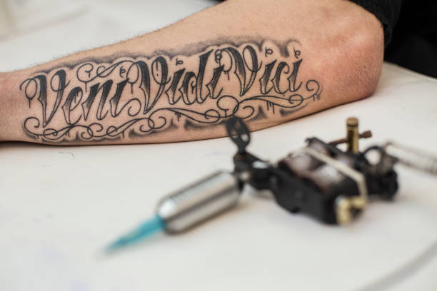 Tattoo Tattoo machine next to a tattoo on a forearm on an unrecognizable Caucasian man. forearm tattoos men stock pictures, royalty-free photos & images