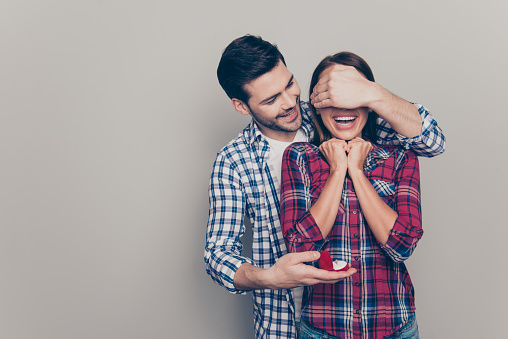 Portrait of handsome beautiful crazy ecstatic laughing lady and positive cheerful glad in casual plaid shirt macho closing face with palm holding small red box with jewellery isolated grey background