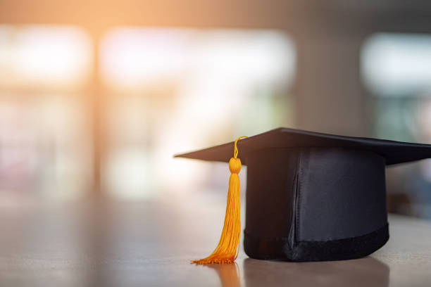 Black hat and yellow tassel of graduates placed on a wooden table Black hat and yellow tassel of graduates placed on a wooden table mortarboard photos stock pictures, royalty-free photos & images