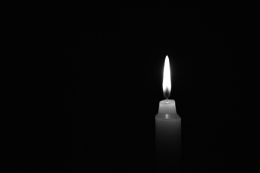 Light candle burning brightly in the black background. Candle flame. There's room for your text. Black and white photo. The concept of mourning, grief or sorrow. Located on the right side of the shot.