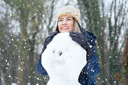 Asian woman enjoying with snow, making snowman in woods