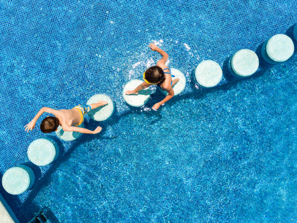 Kids Swimming in a pool Siblings crossing swimming pool on stepping stones people on bridge stock pictures, royalty-free photos & images