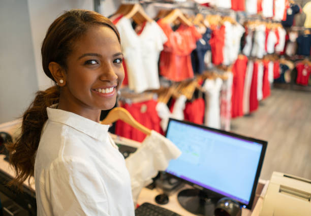 friendly cashier working at a clothing store facing camera smiling - owner boutique store retail imagens e fotografias de stock