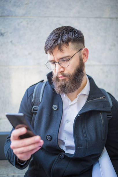 istock Young hipster architect, using mobile phone, sitting in front of the office building 1124475958