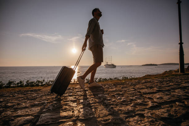 istock Tourist man walking by the sea with suitcase 1124476943