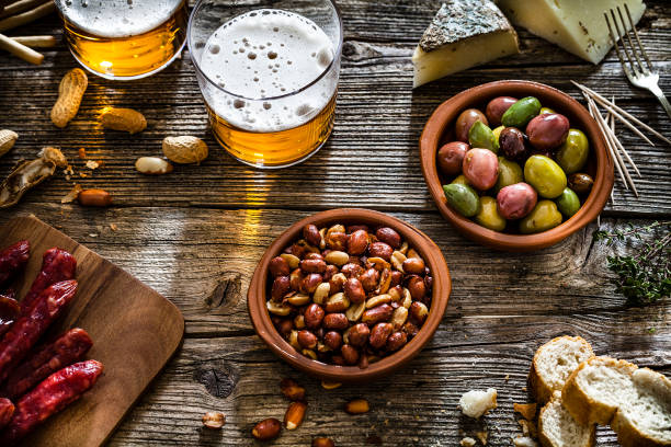 olive, arachidi e birra girate dall'alto su un tavolo rustico in legno - beer nuts foto e immagini stock