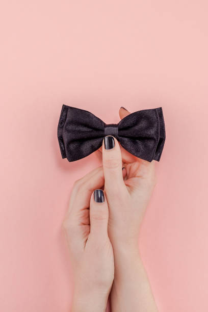 Black bow tie woman hand for men fathers concept Creative flatlay top view retro black bow tie woman hands black manicure pink paper background copy space. Men health awareness month fathers day masculinity valentine holiday concept woman necktie stock pictures, royalty-free photos & images