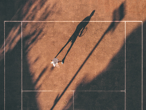 Drone view over tennis court with men in waiting position, hard shadows