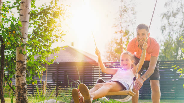 radosny ojciec pcha huśtawki z jego cute córeczka na nich. happy family spędza razem jeden słoneczny letni dzień na idyllicznym podwórku. - outdoors playing family spring zdjęcia i obrazy z banku zdjęć