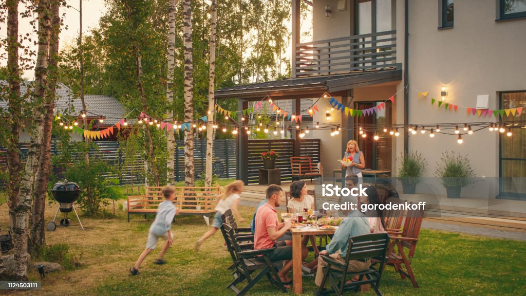 Grande família jardim festa celebração, reunida na mesa de família, amigos e crianças. As pessoas estão bebendo, passando de pratos, Joking e Having Fun. Crianças correr ao redor da mesa. - Foto de stock de Família royalty-free