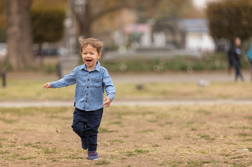Cute boy in blue shirt running in the park. Selective focus.