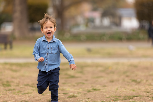 Cute boy in blue shirt running in the park. Selective focus.
