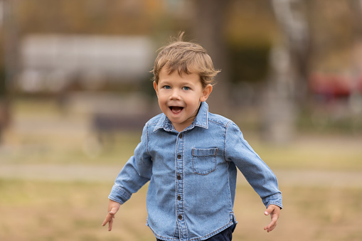 Cute boy in blue shirt running in the park holding out his arms. Selective focus.