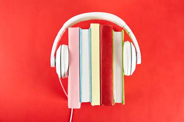 Photo of Audio vs. paper book concept. Reading versus listening. Books and headphones on table.