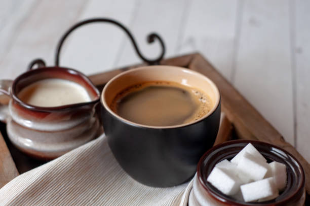 Black ceramic coffee mug with ceramic creamer and sugar bowl set on wooden serving tray.