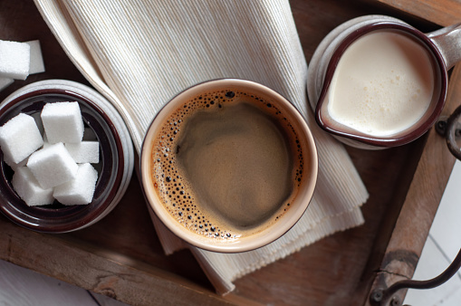 Black ceramic coffee mug with ceramic creamer and sugar bowl set on wooden serving tray.