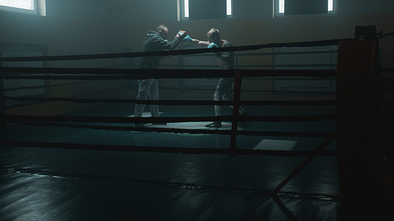 Tattooed boxer sparring with his trainer in boxing ring.
