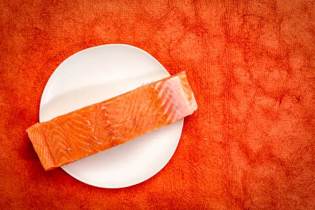 raw, wild king salmon fillet on a white plate against red texture background