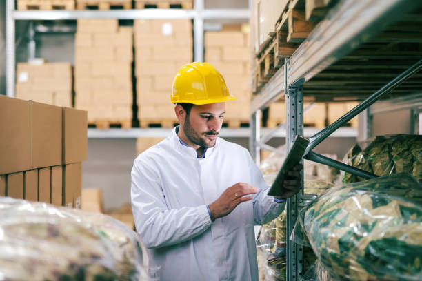 istock Unshaven serious man in uniform and helmet on head using tablet for work. Storage interior. 1124533170