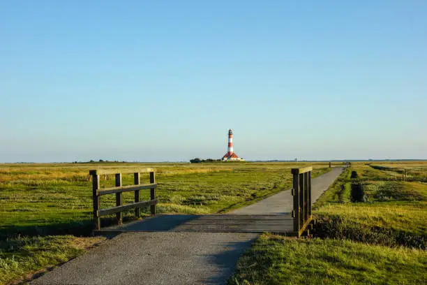 Westerhever lighthouse with path in salt marshes at blue sky