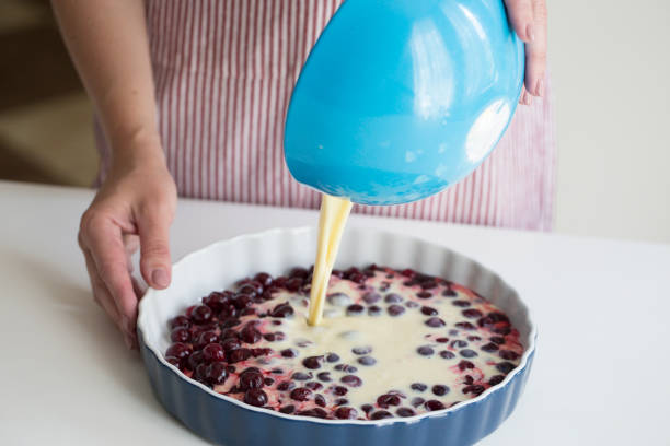 jeune femme de cuisson dans la cuisine. tarte clafoutis cerise. préparation d’un gâteau français aux cerises - pie fruit cobbler sweet food photos et images de collection