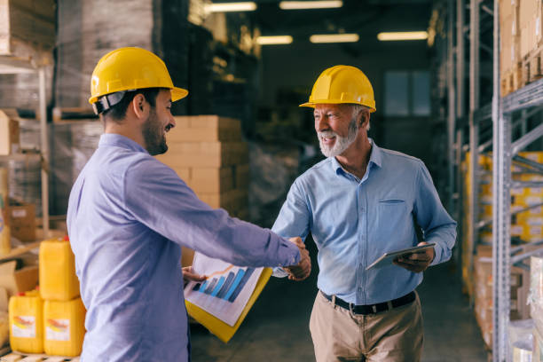 dos hombre de negocios con cascos de cabeza agitando las manos para bien terminado. interior de almacenamiento. - manual worker handshake industry warehouse fotografías e imágenes de stock