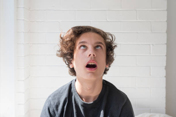 Teen boy rolling eyes and looking up Head and shoulders view of teenage boy rolling eyes and looking up at ceiling (selective focus) rolling eyes stock pictures, royalty-free photos & images