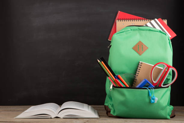 istock Education concept - school backpack with books and other supplies, blackboard background 1124545536